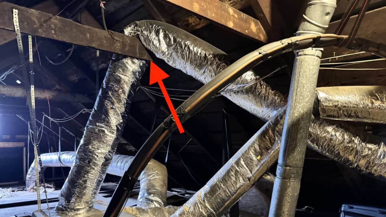 Flexible HVAC ductwork hanging over roof rafters in a home attic.